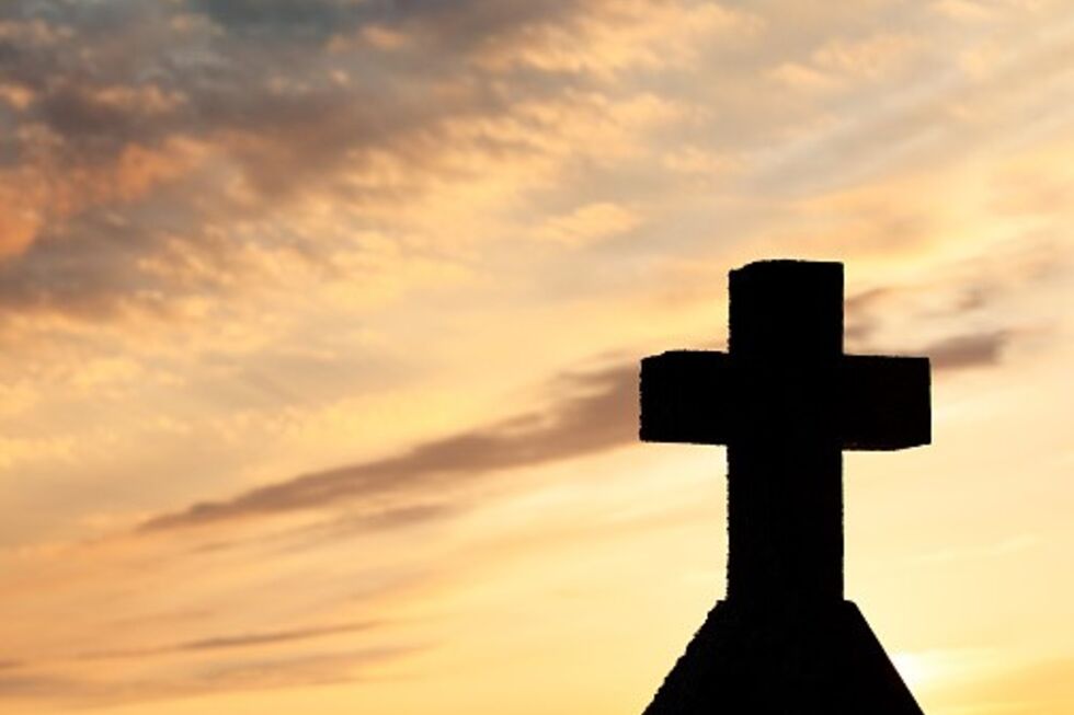 Cruz de silhueta contra um céu com nuvens coloridas ao pôr do sol