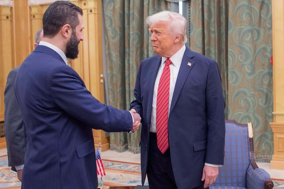 Nesta foto postada pelo Palácio Saudita, o presidente Donald Trump aperta as mãos do presidente sírio interino de Riad, Ahmad Al-Sharaa. 
