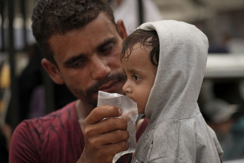 Homem dá água a criança, em situação de possível subnutrição, em Gaza