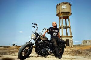 Homem com t-shirt 'Sarony Lisboa' posa com mota, junto a torre de água