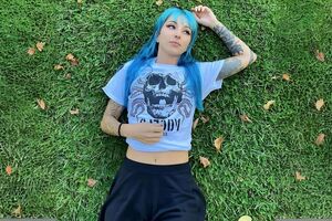 Mulher com cabelo azul e tatuagens relaxa na relva