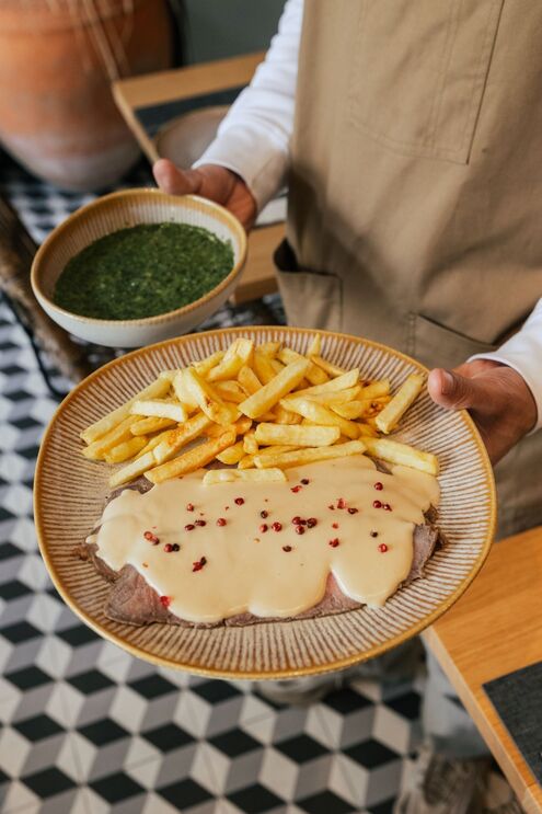 Prato com bife, molho, pimenta rosa e batatas fritas, servido por um empregado de mesa