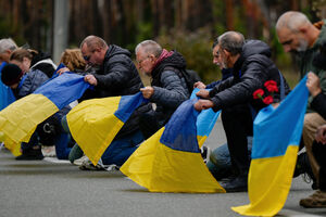 Pessoas ajoelhadas com a bandeira da Ucrânia em homenagem aos soldados mortos