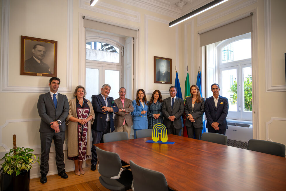 Grupo de pessoas posa para foto numa sala com bandeiras de Portugal