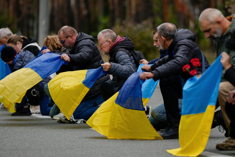 Pessoas ajoelhadas com a bandeira da Ucrânia em homenagem aos soldados mortos