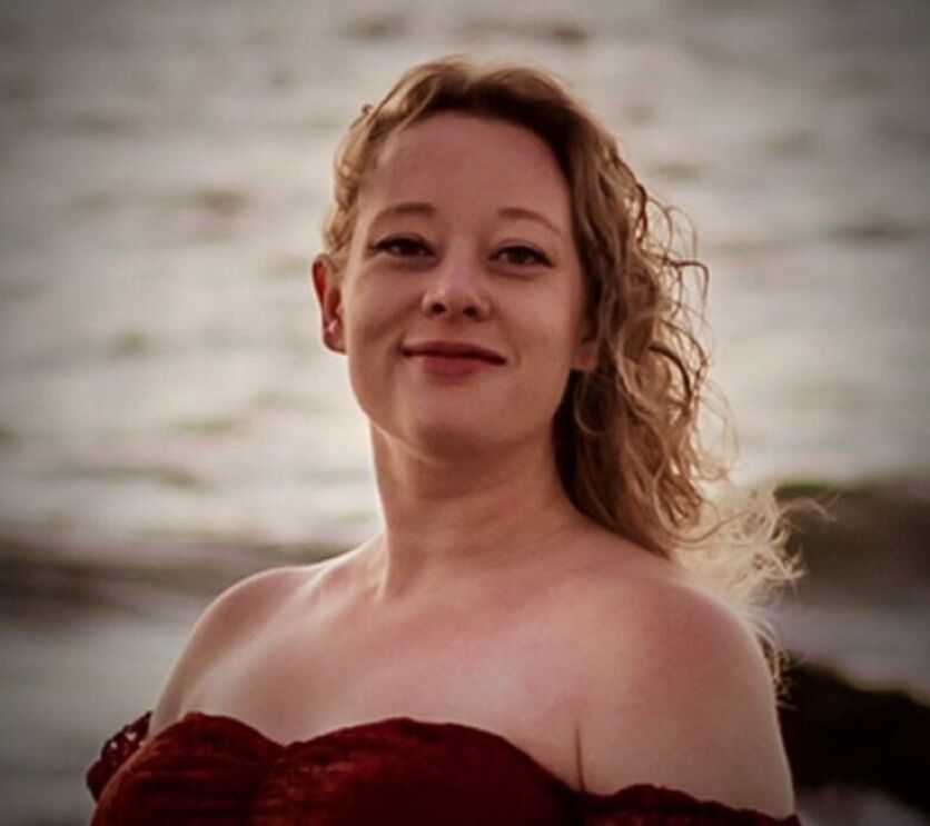 Mulher sorri com vestido vermelho em frente ao mar