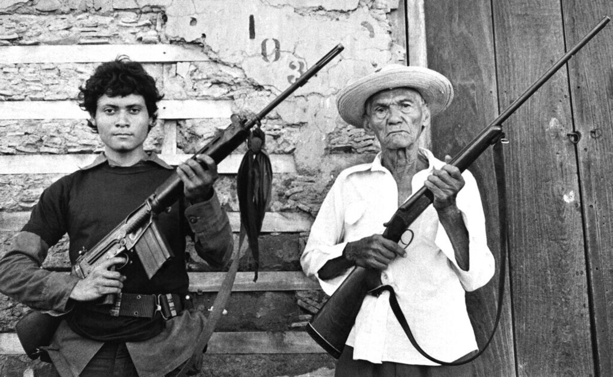 Um veterano de 87 anos da primeira rebelião de Sandino, armado com uma espingarda ao lado de um guerrilheiro sandinista de 18 anos em León, Nicarágua