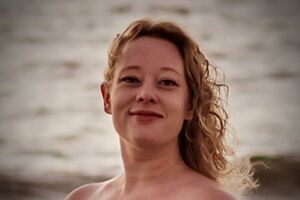 Mulher sorri com vestido vermelho em frente ao mar