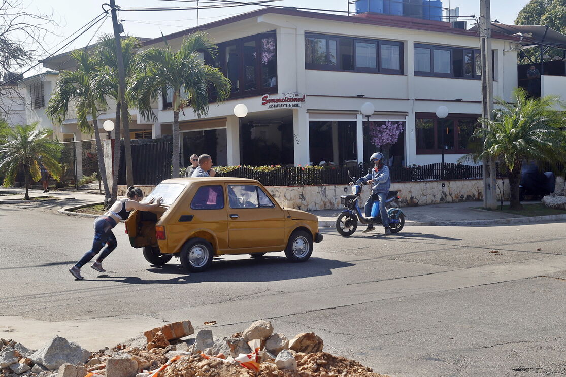 Mulher empurra carro em Havana