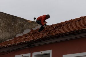 Homem repara telhado danificado pela tempestade Kristin em Portugal