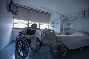 Doente em cadeira de rodas num quarto de hospital do SNS, aguardando reabilitação