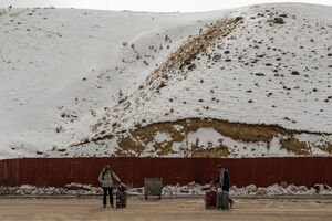 Pessoas com malas aguardam transporte em zona montanhosa coberta de neve
