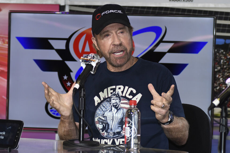Chuck Norris discursa ao lado de um microfone e uma garrafa de água