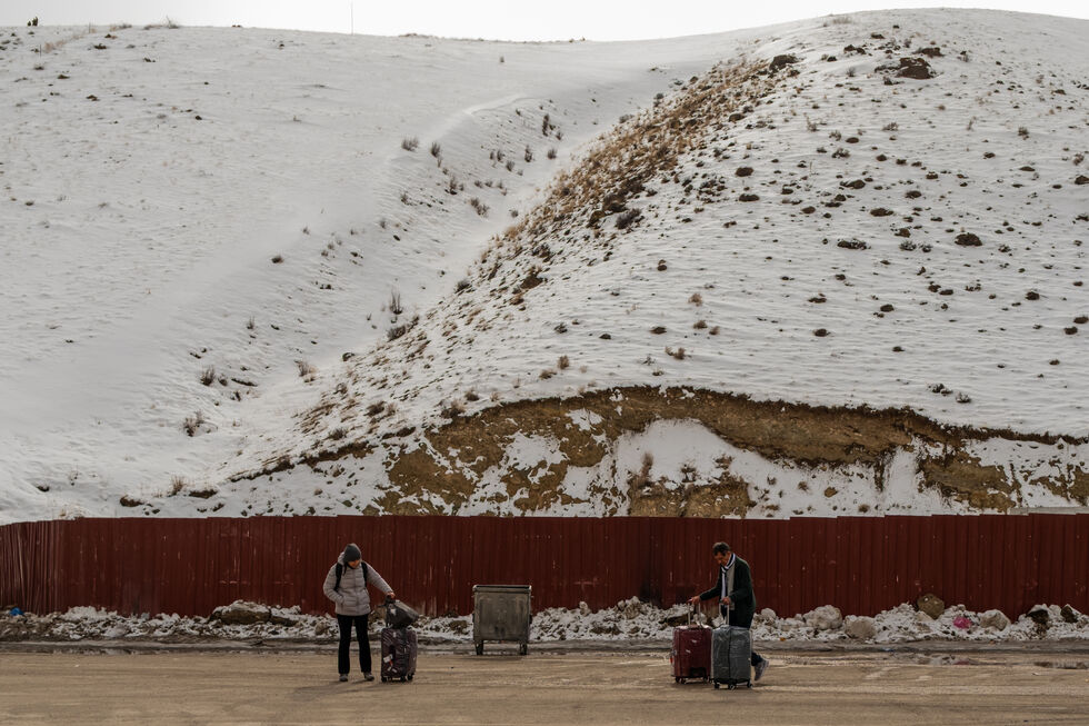 Pessoas com malas aguardam transporte em zona montanhosa coberta de neve