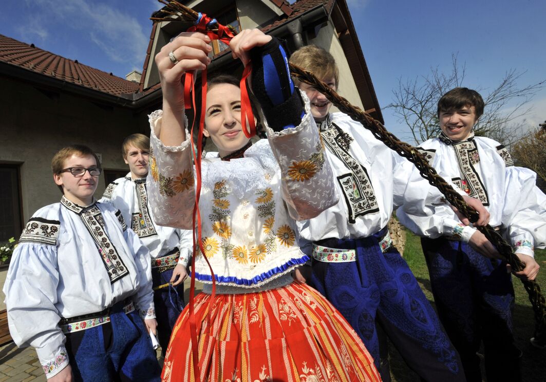 Jovens em trajes folclóricos chicoteiam uma menina 