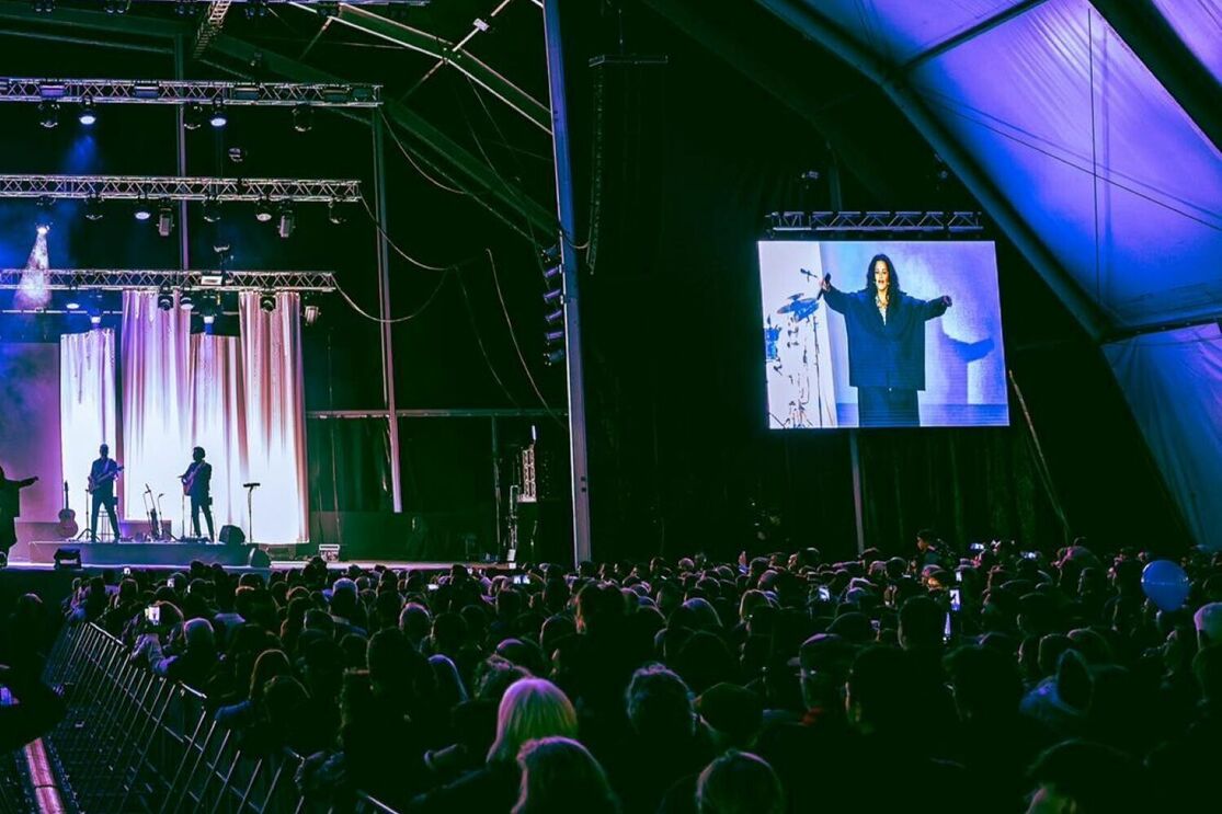 Concerto com artista no ecrã e banda no palco para uma multidão