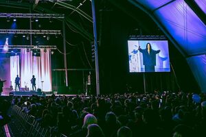 Concerto com artista no ecrã e banda no palco para uma multidão