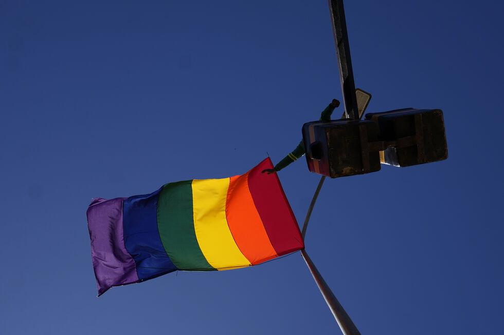 Bandeira LGBTQIAP+ hasteada num poste sob um céu azul