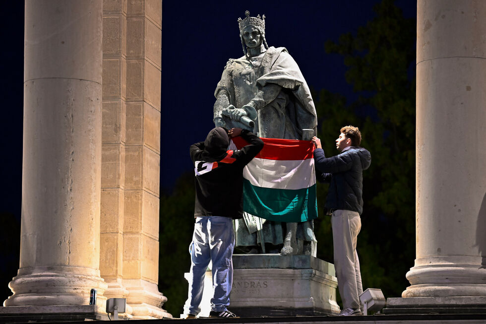 Manifestantes exibem bandeira da Hungria em frente à estátua de Rei André I, em Budapeste