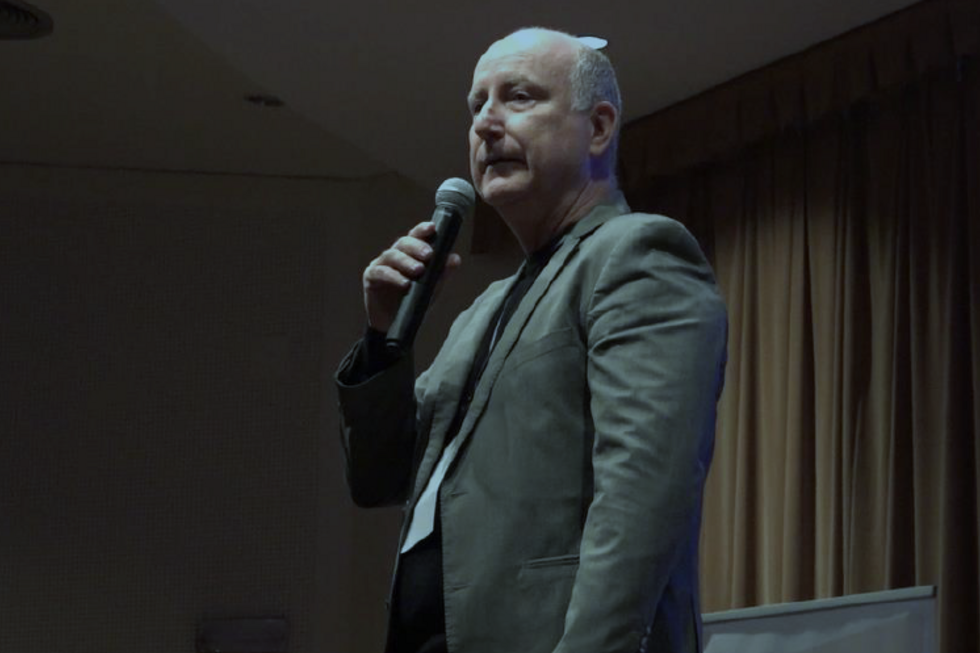 Homem discursa ao microfone num palco com cortinas