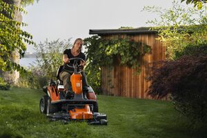 Mulher corta relva num grande jardim com máquina motorizada