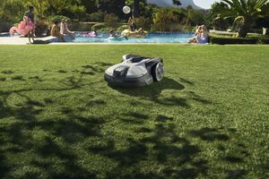 Um robô corta relva num jardim onde pessoas aproveitam uma piscina