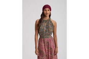 Mulher posa com vestido comprido e padrão paisley, e usa um gorro vermelho