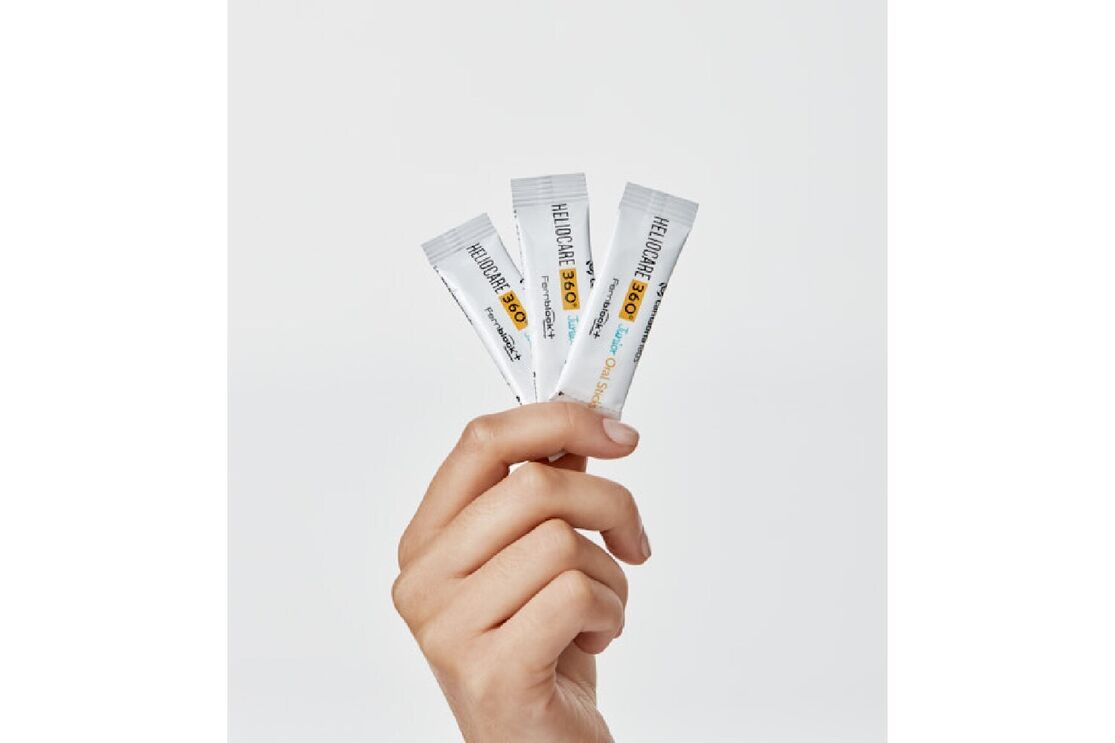 Mão segura 3 ampolas de Heliocare 360º Junior Oral Sticks