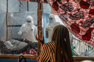 Pessoas em trajes de proteção cuidam de um doente em surto de Ébola