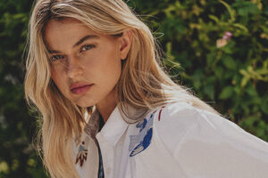 Mulher com camisa branca bordada com flores e padrão xadrez ao fundo