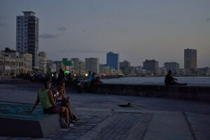 Duas jovens usam telemóveis junto ao mar em Havana