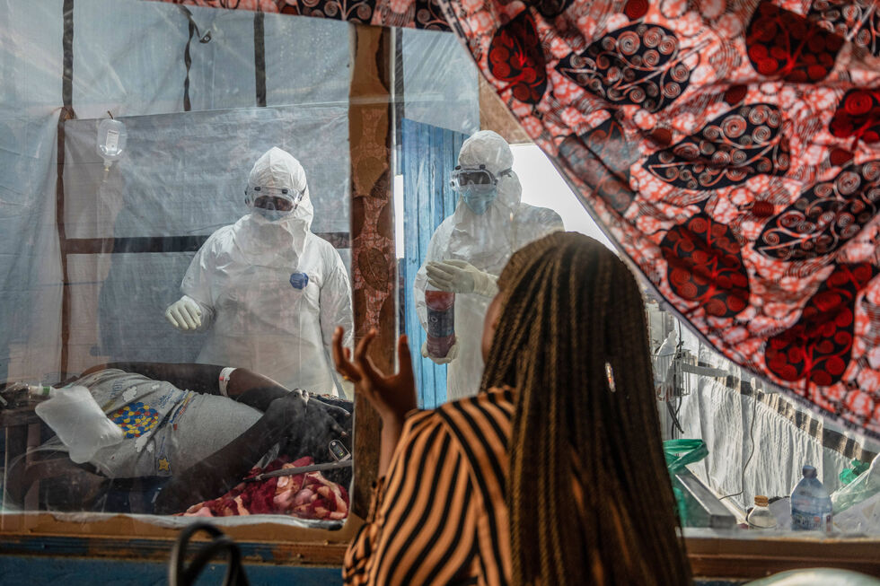 Pessoas em trajes de proteção cuidam de um doente em surto de Ébola