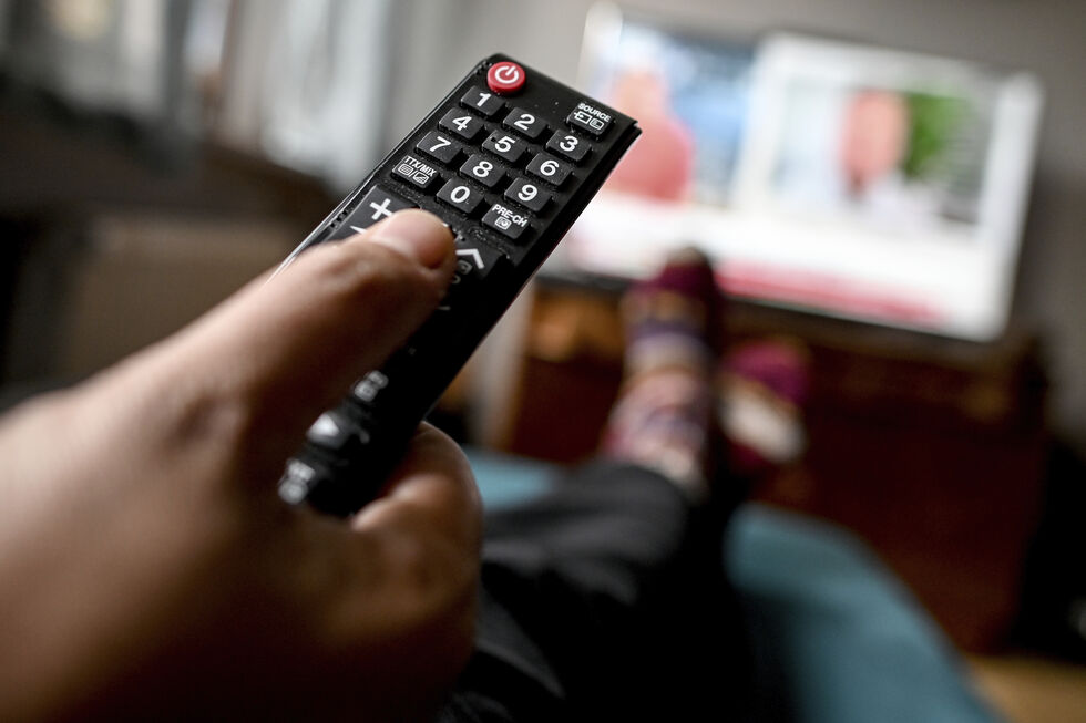 Pessoa a ver televisão com um comando na mão