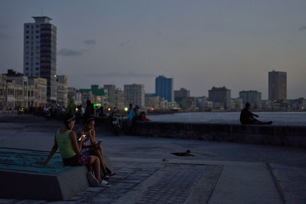 Duas jovens usam telemóveis junto ao mar em Havana