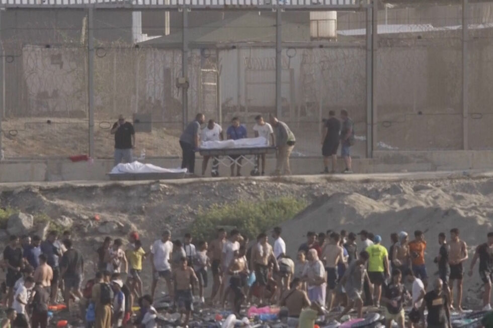 Perto da fronteira de Ceuta, corpos são transportados numa maca enquanto migrantes observam