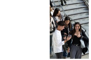Estudantes em escadas, um a mostrar o telemóvel a outros