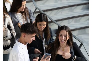 Estudantes em escadas, um a mostrar o telemóvel a outros