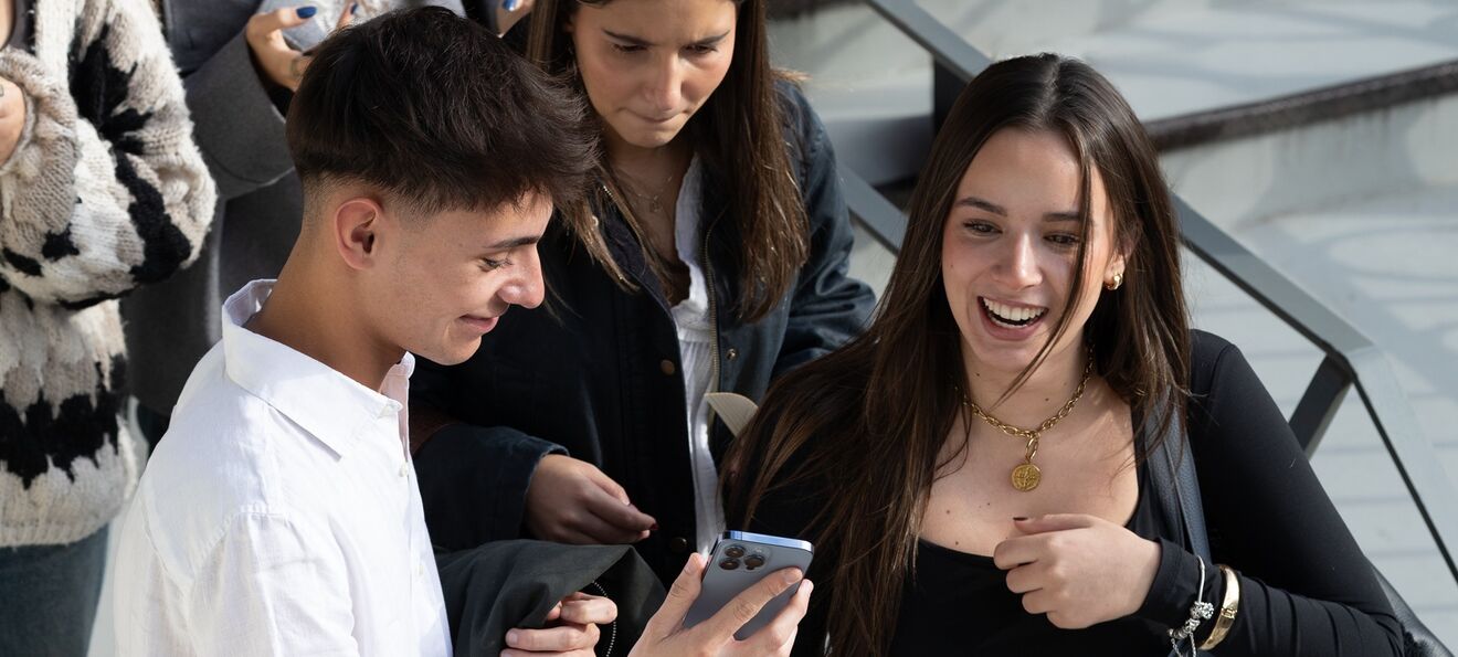 Estudantes em escadas, um a mostrar o telemóvel a outros