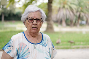 Senhora idosa com cabelos brancos e óculos olha para a câmara