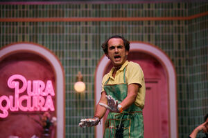 Um ator em palco grita, com "Pura Loucura" em neon no fundo