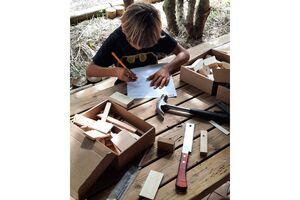 Criança desenha projeto de construção em mesa de madeira com ferramentas e peças de madeira