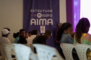 Pessoas em frente a um banner da Estrutura Missão AIMA