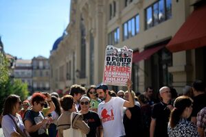 Pessoas em protesto com cartaz "O Porto não se vende" em frente a edifícios